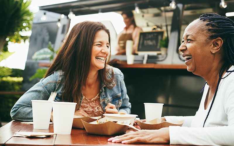 image of two women laughing in front of  a food truck